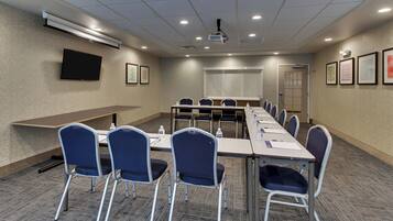 A conference room with a long table, chairs, a projector, and a screen.