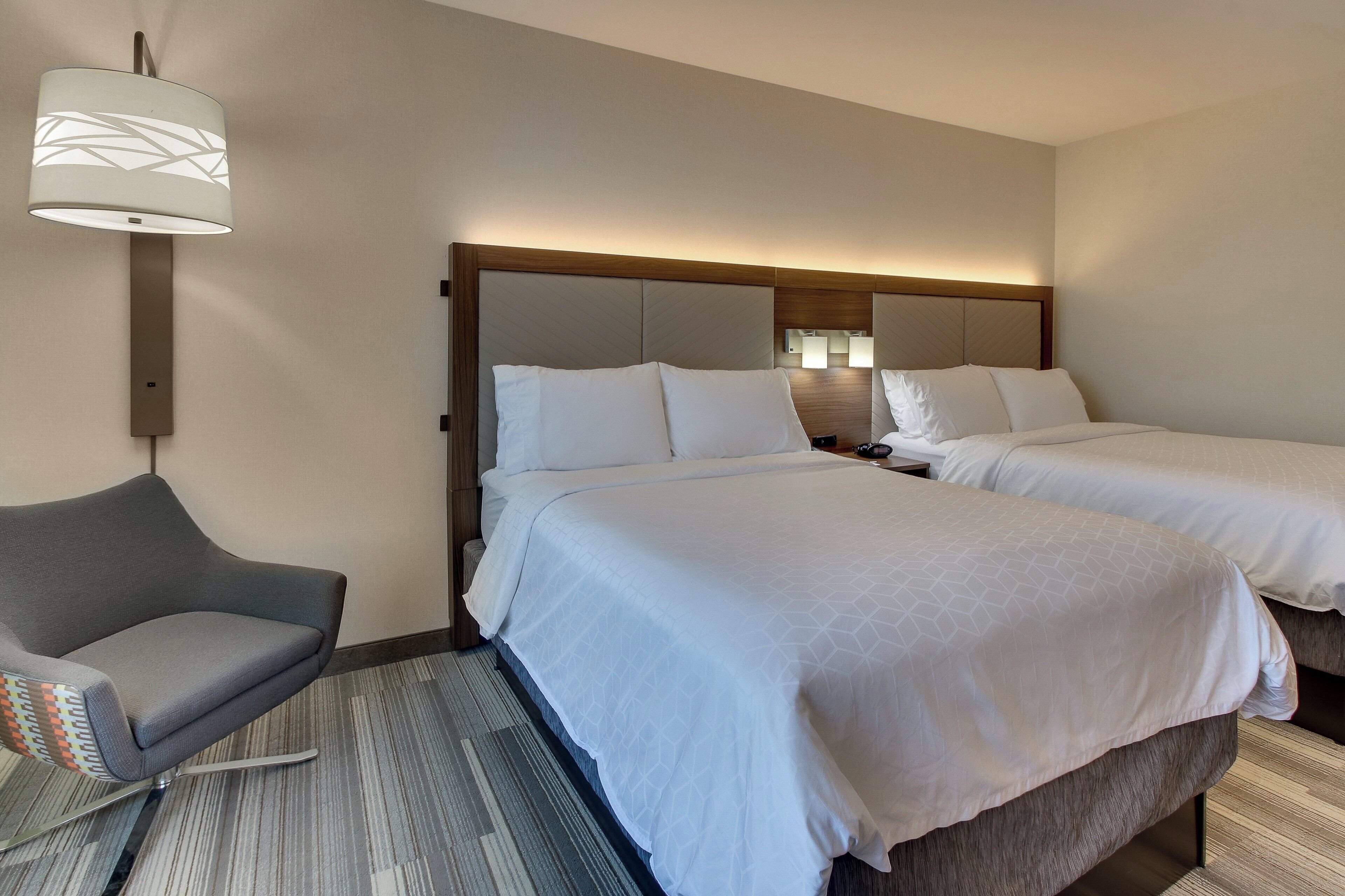 Ein Hotelzimmer mit zwei Betten, einem Sessel, einer Lampe und Teppichboden.