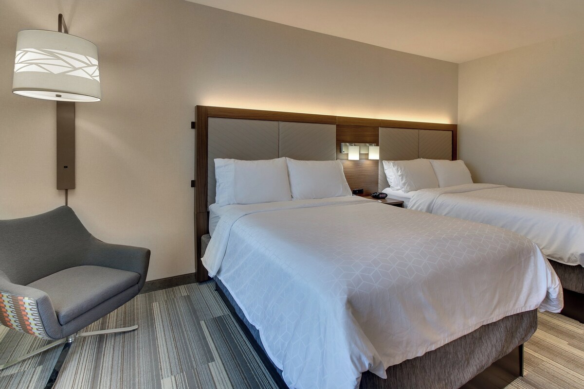 Een hotelkamer met twee bedden, een stoel, een lamp en een vloerbedekking.