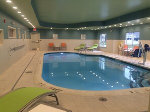 An indoor swimming pool with clear water, surrounded by lounge chairs and a lifeguard station.