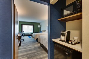 A hotel room with a bed, a desk with a coffee maker, a microwave, and a view of the city.