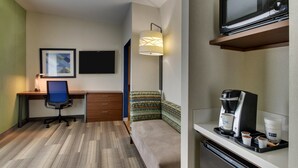 Quarto de hotel compacto com escrivaninha, cadeira, cama e pequeno espaço de cozinha.