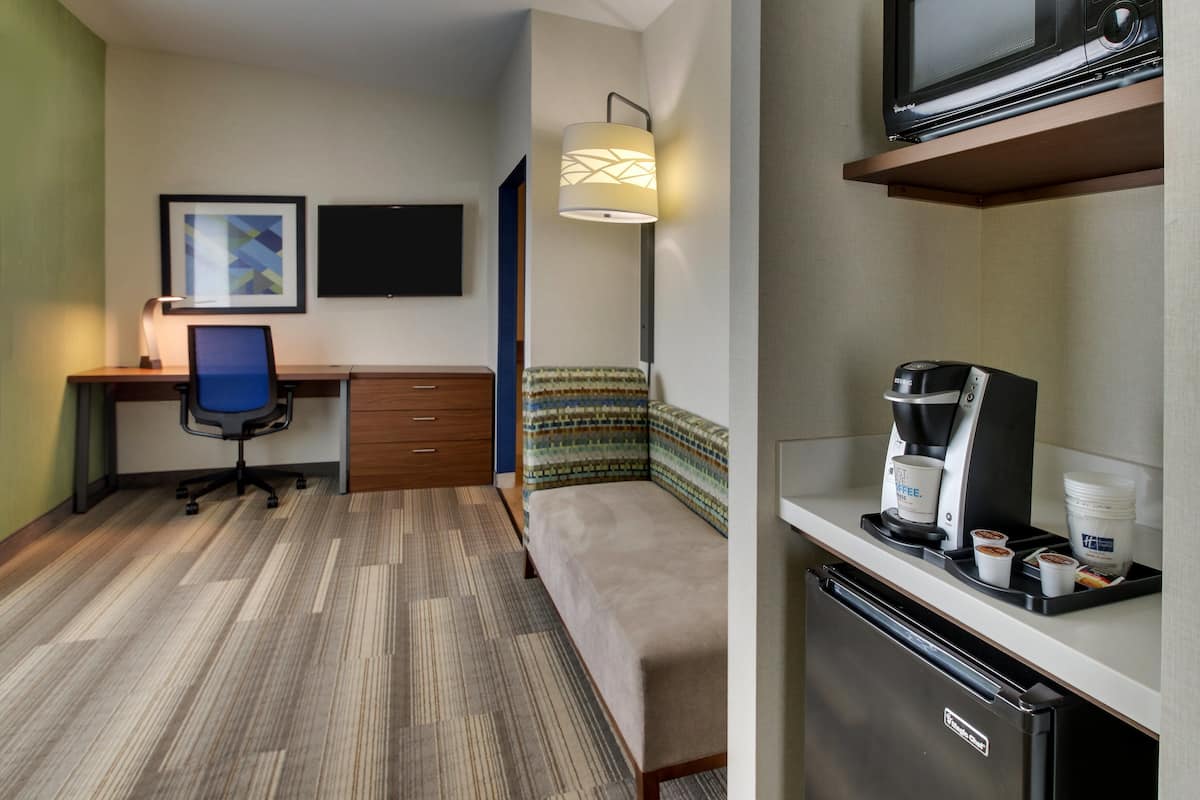 A compact hotel room with a desk, chair, bed, and kitchenette.