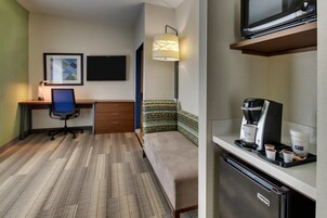 Una habitación de hotel funcional con escritorio, silla, cama y kitchenette.