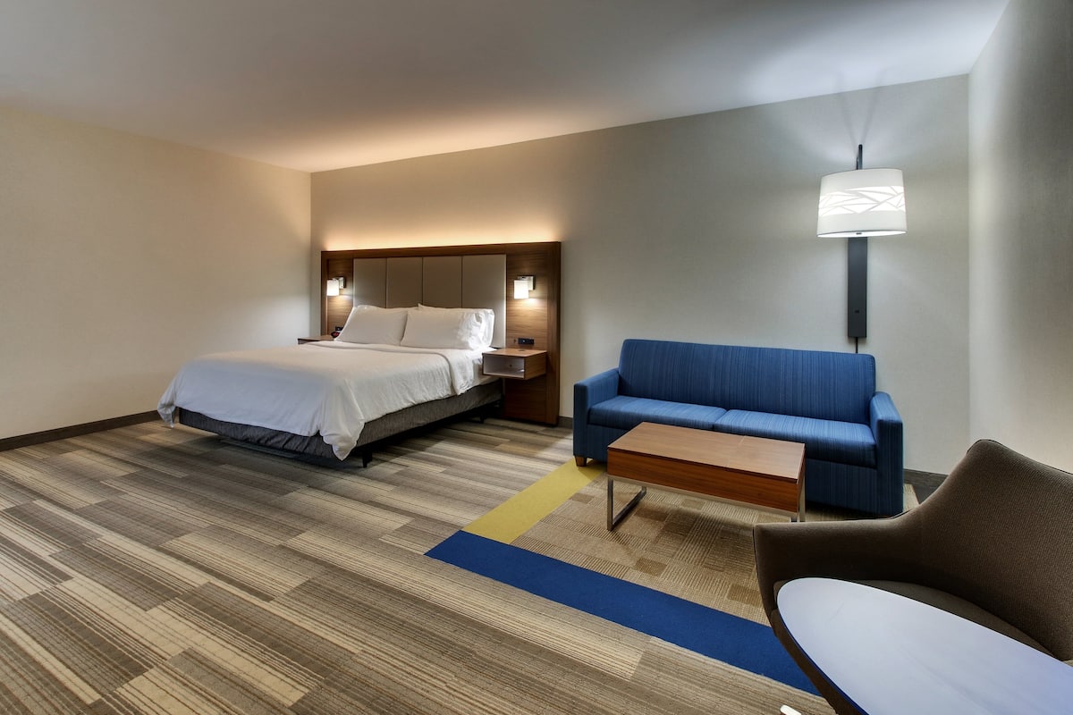 A hotel room with a bed, a blue sofa, a wooden coffee table, and a lamp.