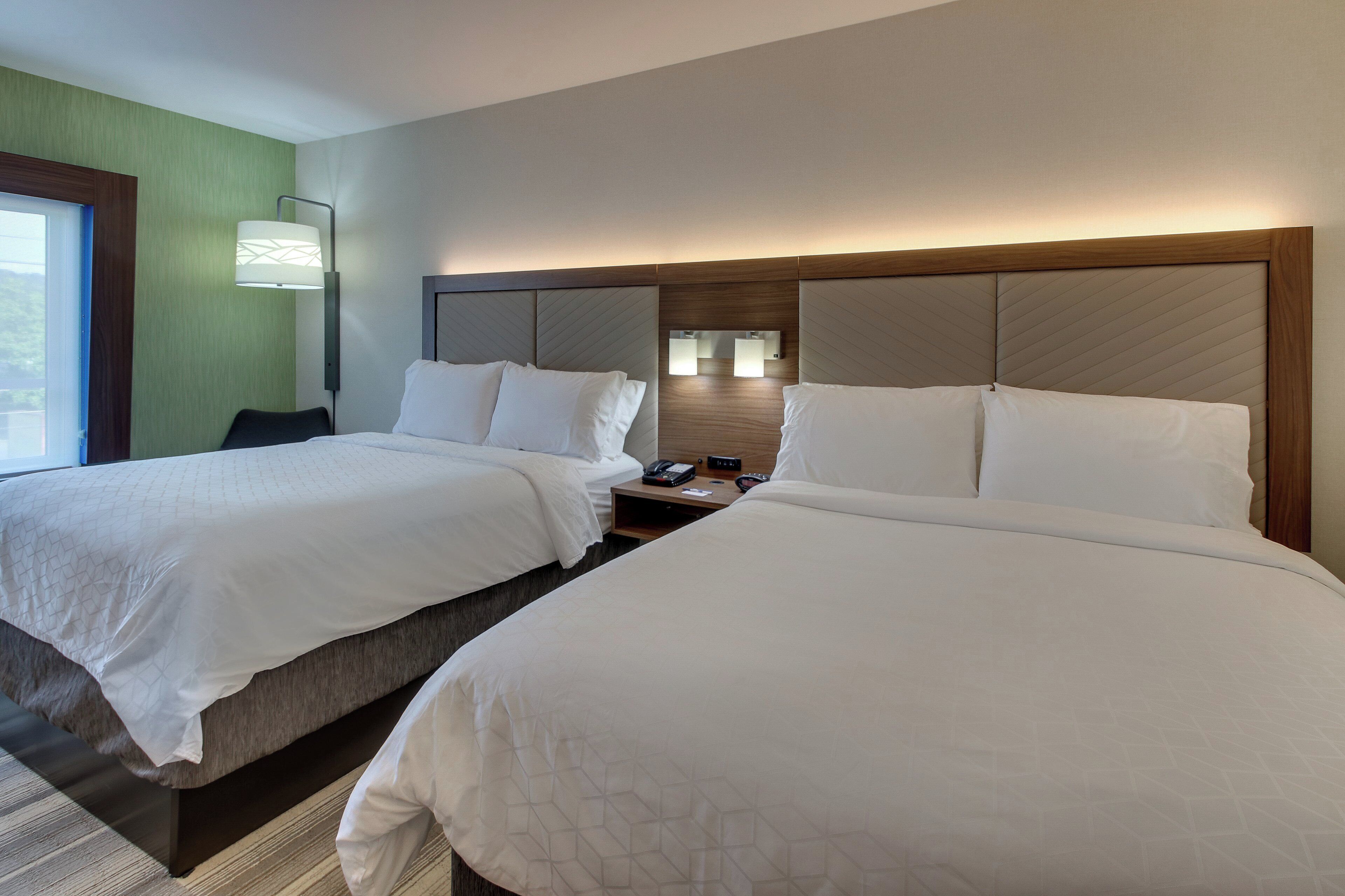 Een hotelkamer met twee bedden, een nachtkastje met een lamp en uitzicht op het omliggende landschap.