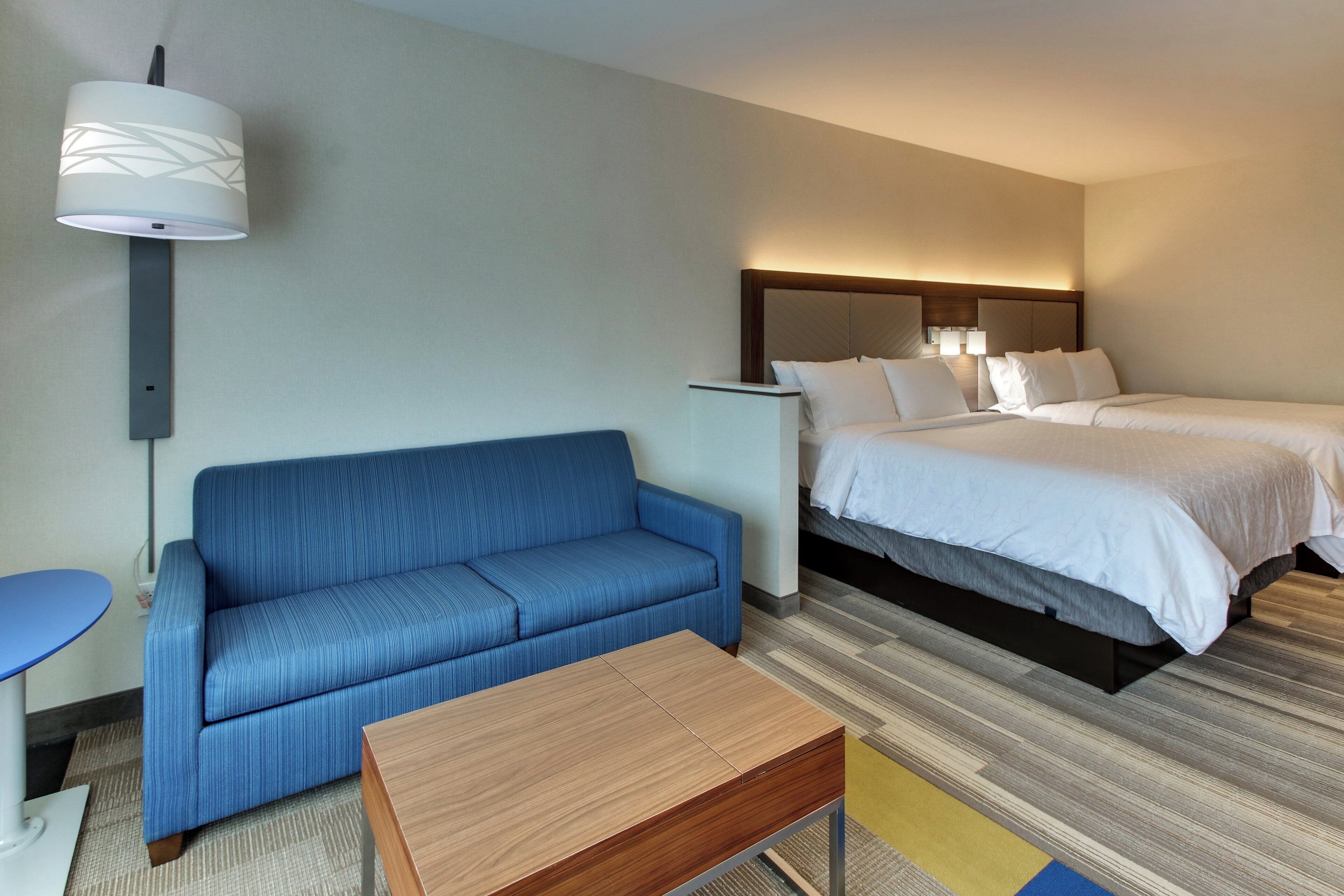 Una habitación de hotel con una cama, un sofá azul, una mesa de madera y una lámpara.