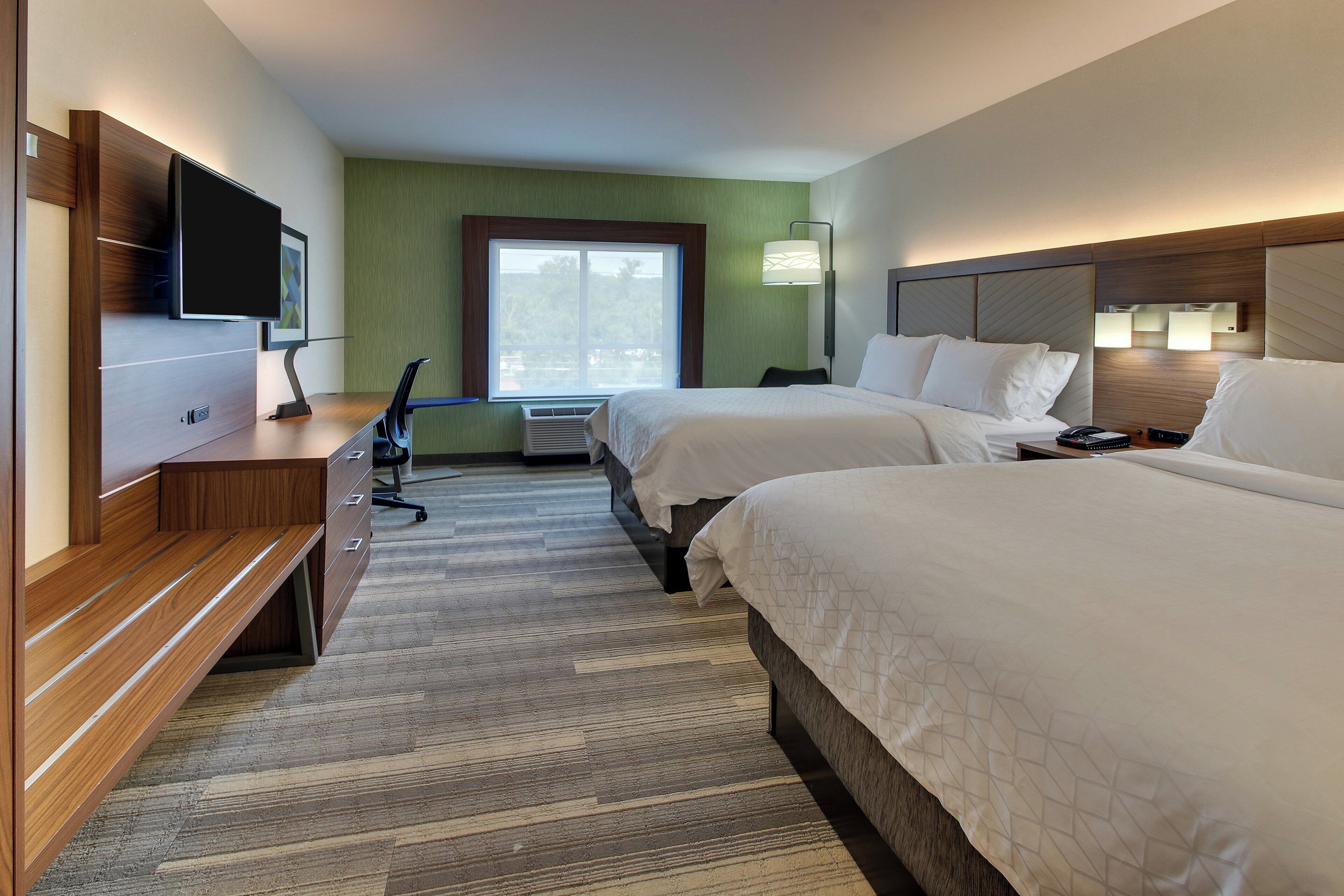 A hotel room with two beds, a desk with a flat-screen TV, a chair, and a large window.