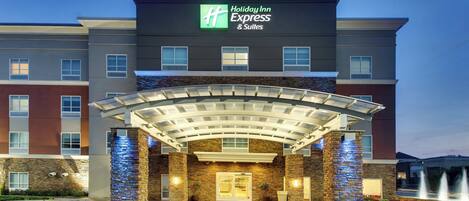 Ein Holiday Inn Express & Suites Hotel mit überdachter Einfahrt und einem begrünten Vordergrund.