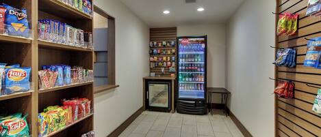 A snack and beverage area with shelves stocked with various snacks, a refrigerator, and a vending machine.
