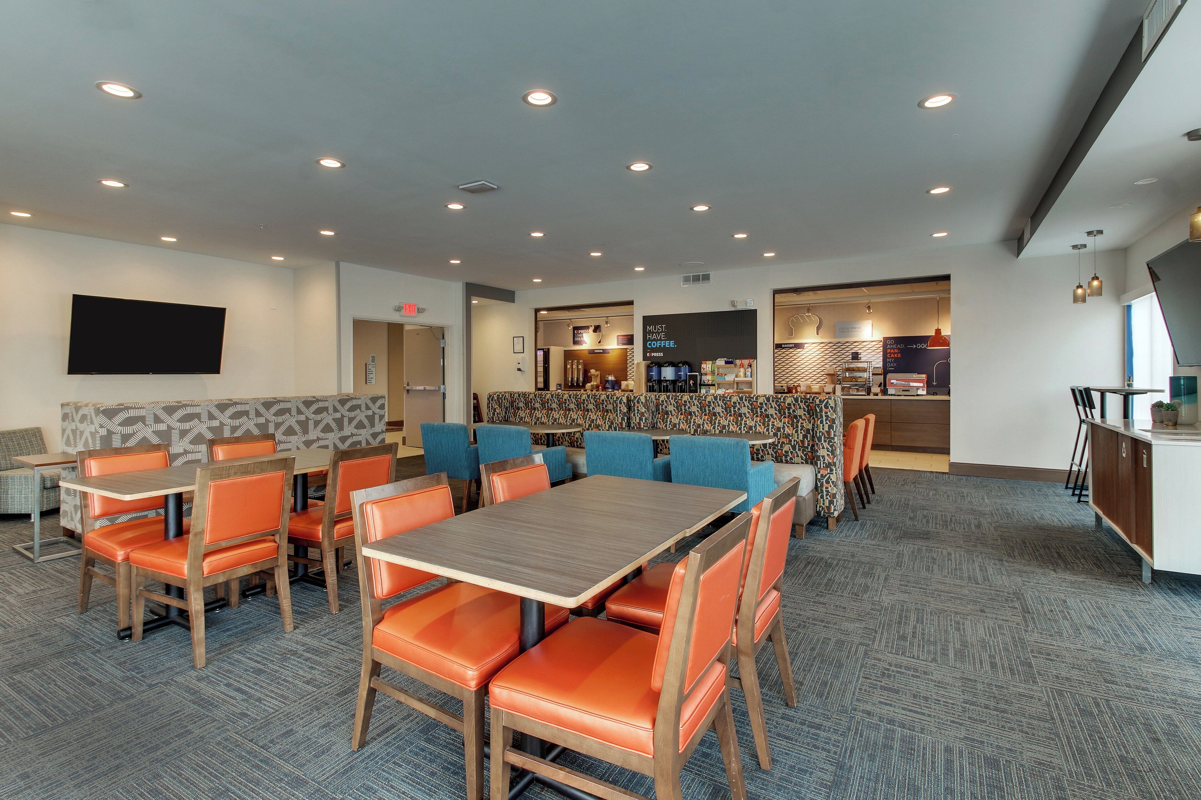 A modern hotel dining area with a mix of seating options, including tables and booths, and a visible coffee bar in the background.
