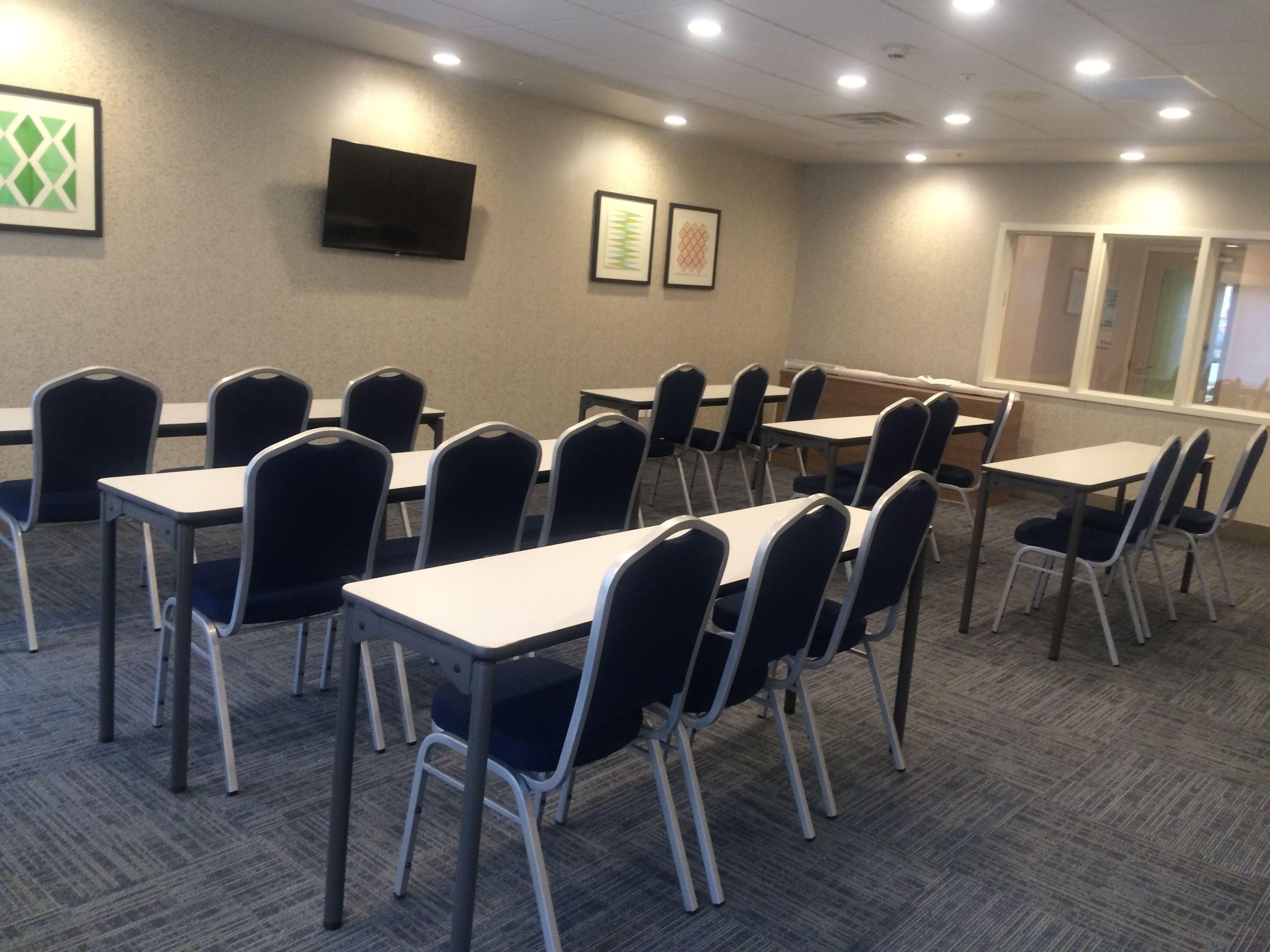 A conference room with tables and chairs, a flat-screen TV on the wall, and framed artwork.