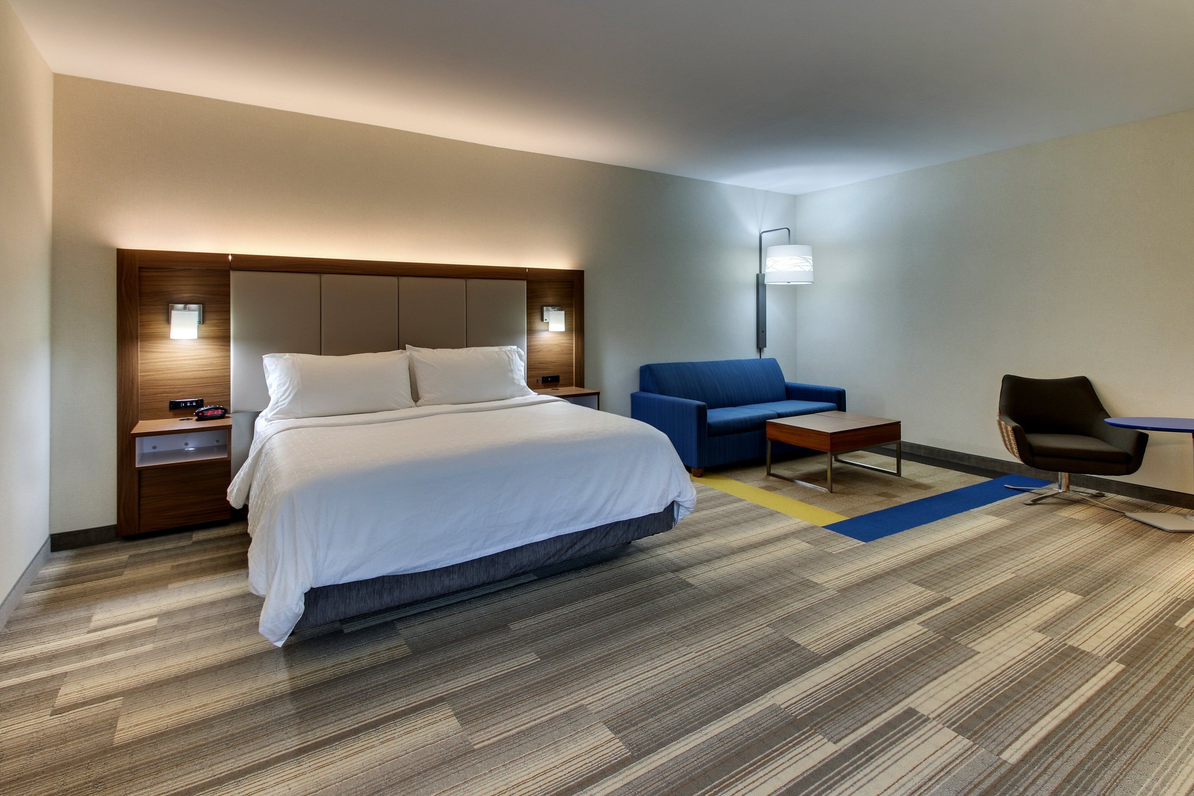 A modern hotel room with a large bed, a blue sofa, a small table, and a chair.
