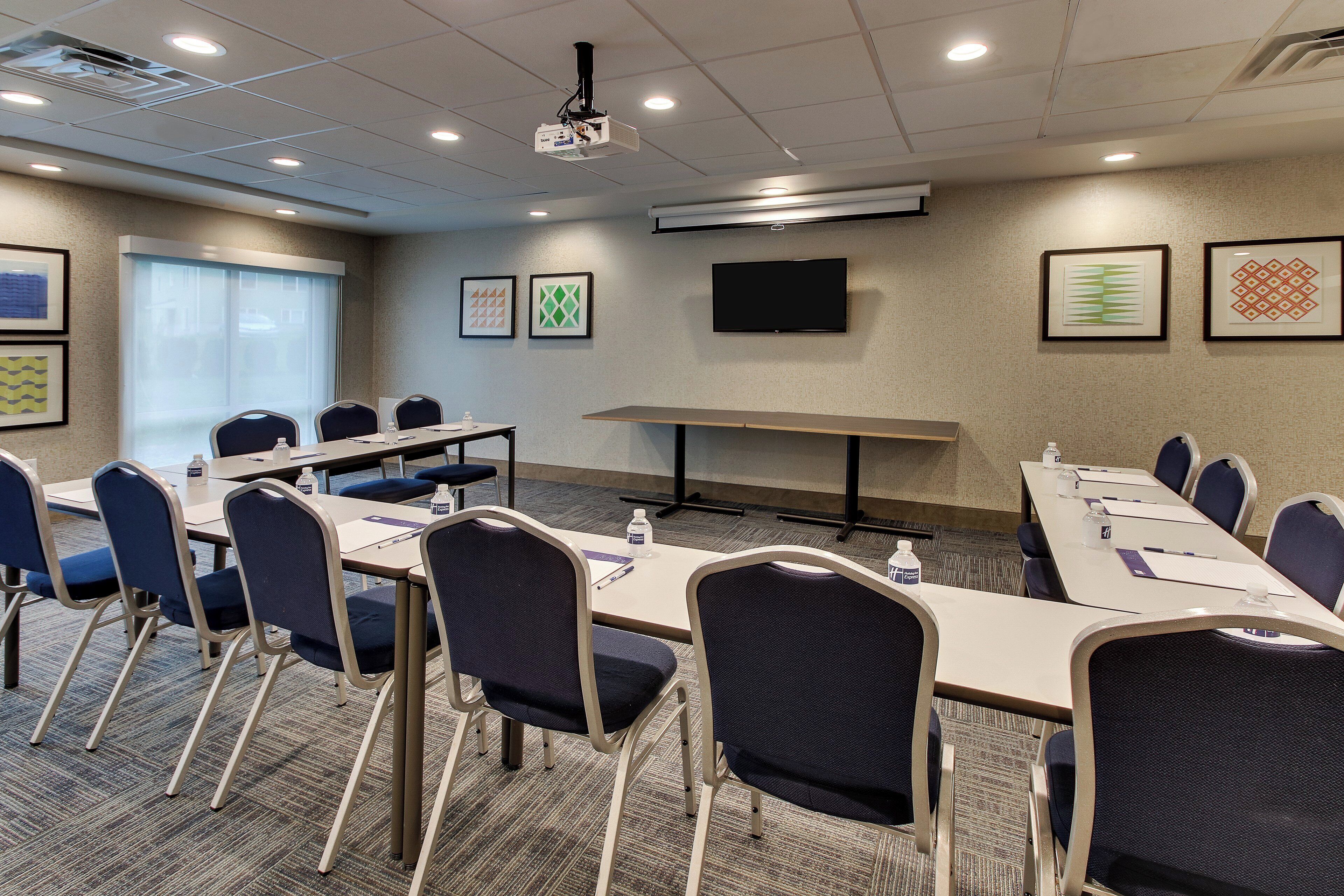A conference room with a long table, chairs, a projector, and framed artwork on the walls.
