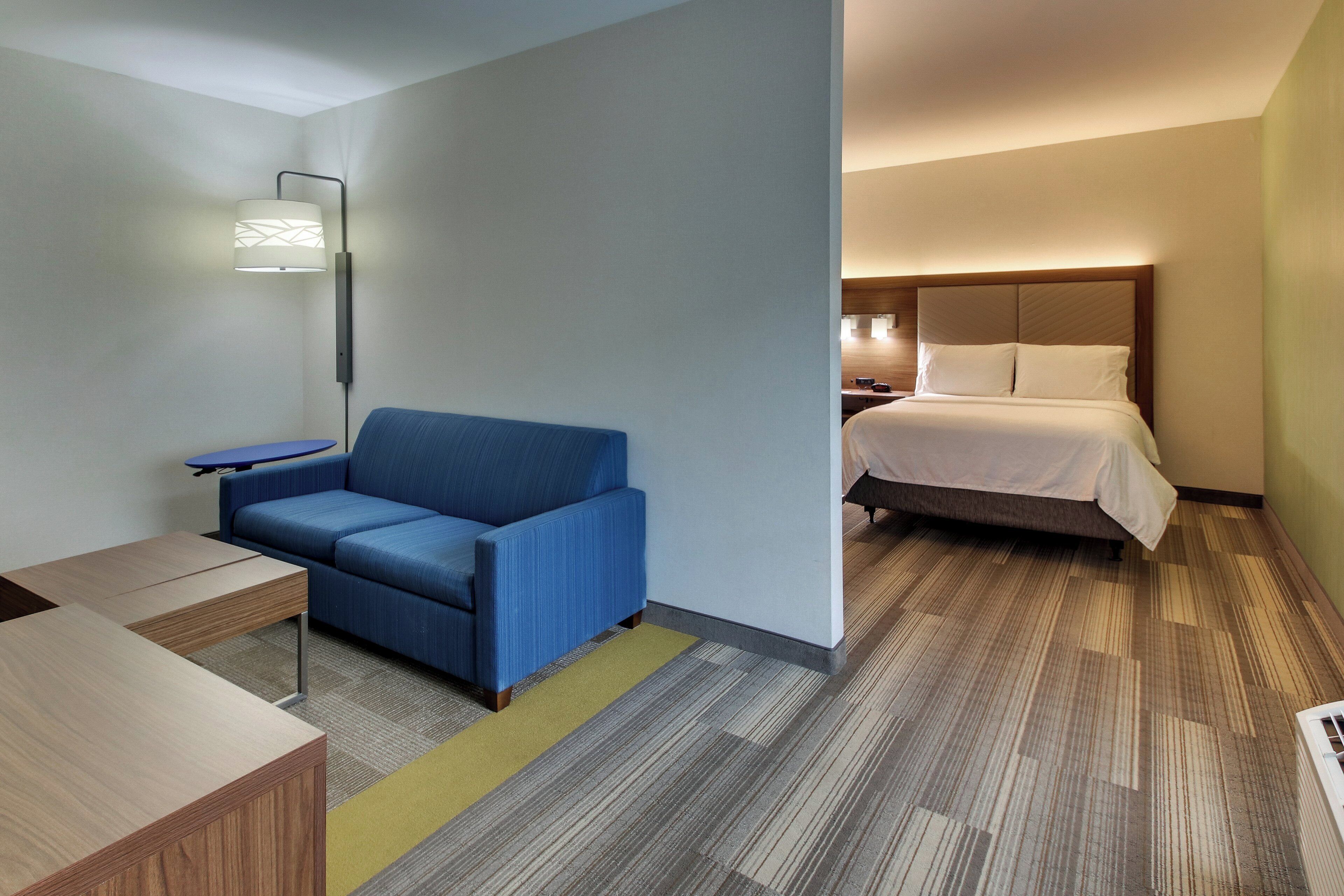 A hotel room with a blue sofa, a small table, a bed with white bedding, and a floor lamp.