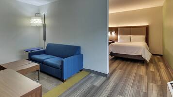 A hotel room with a blue sofa, a small table, a bed with white bedding, and a floor lamp.
