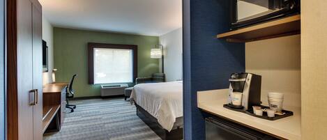 A hotel room with a bed, desk, microwave, coffee maker, and a view of a cityscape.