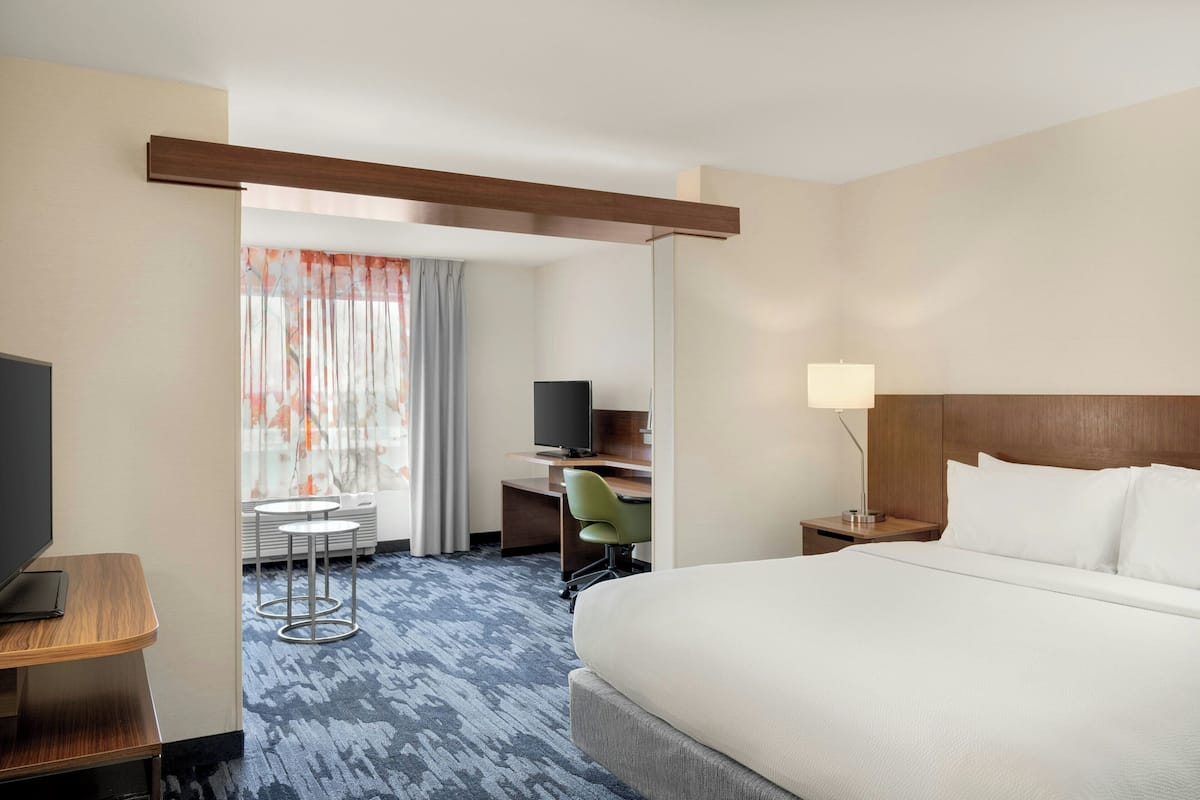 A hotel room with a large bed, a desk with a computer, a TV, a small table, and a chair.