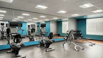 Un gimnasio con diferentes máquinas de ejercicio, un espejo grande y una ventana con persianas.
