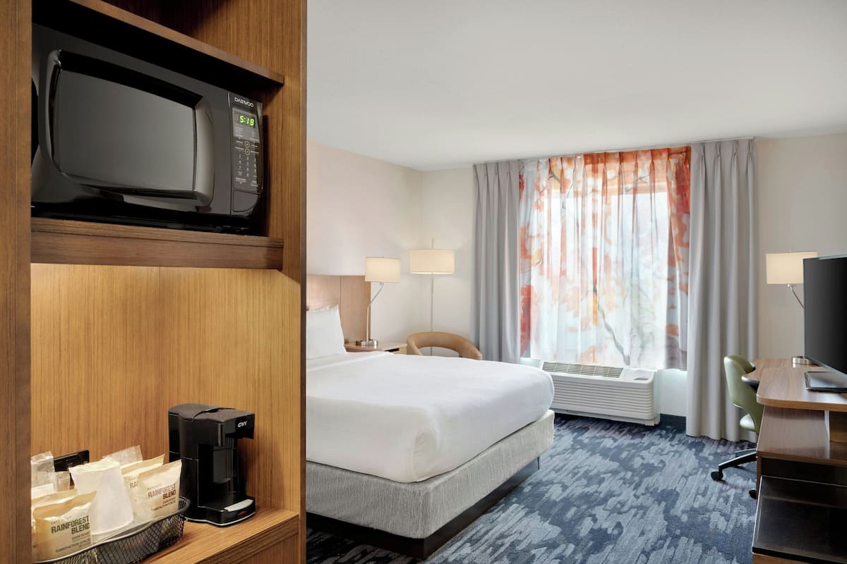 A hotel room with a bed, a desk, a TV, a coffee maker, and a window with curtains.
