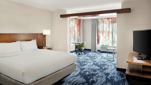 A hotel room with a large bed, a desk with a chair, a television, and a window with curtains.