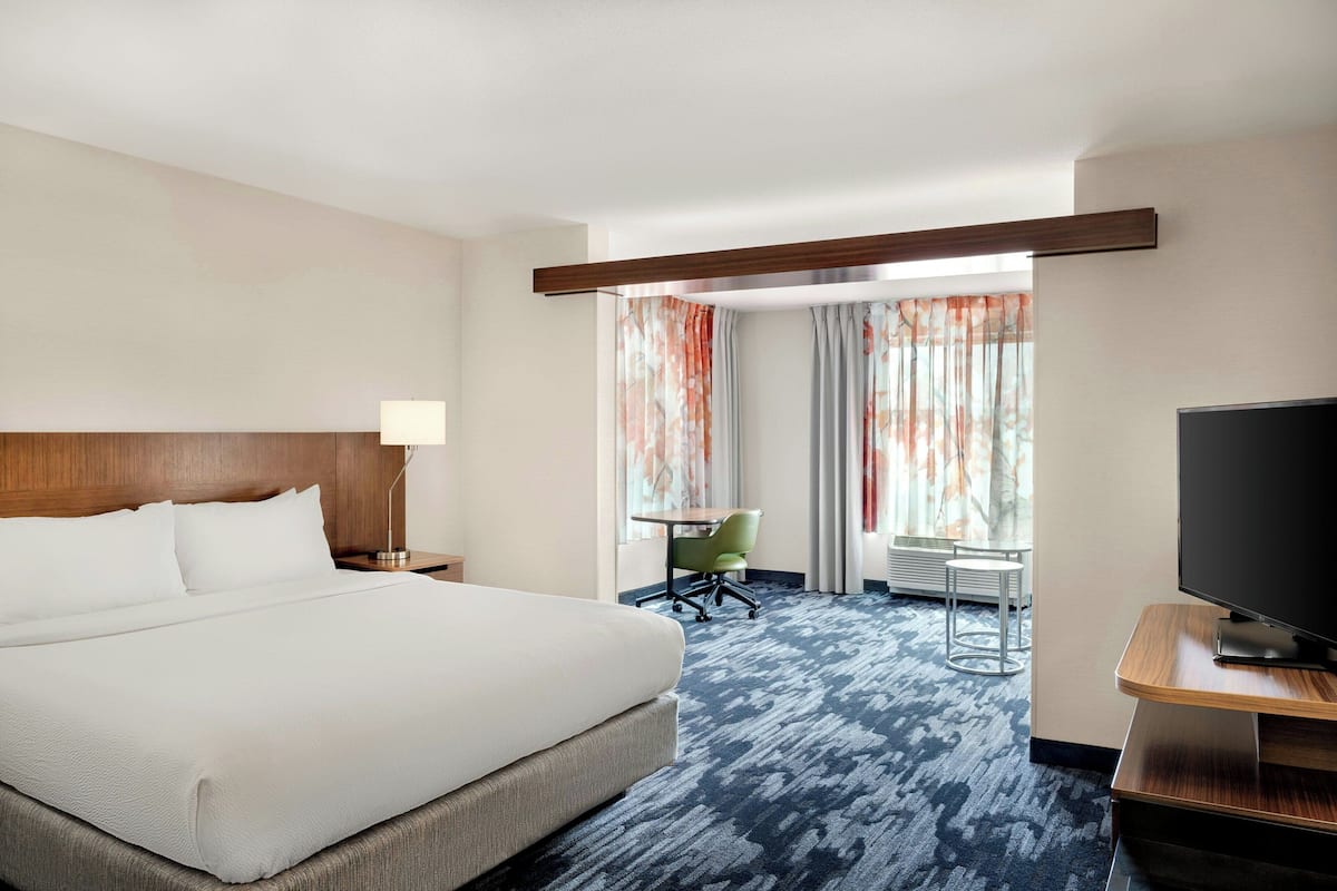 A hotel room with a large bed, a desk with a chair, a television, and a window with curtains.