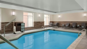 A swimming pool with a sunlit area, a sun porch with chairs, and a small table.