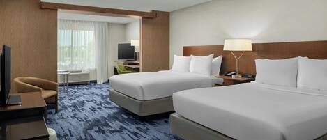 A hotel room with two beds, a desk with a chair, a television, and a lamp.