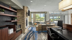 Un espace de bureau moderne avec un mur d’accent en pierre, une grande fenêtre donnant sur un paysage verdoyant, un bureau avec un ordinateur et un coin salon avec un canapé et des fauteuils.