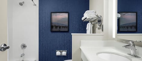 Un baño moderno con pared azul texturizada, una bañera blanca, un lavamanos con espejo y un inodoro.