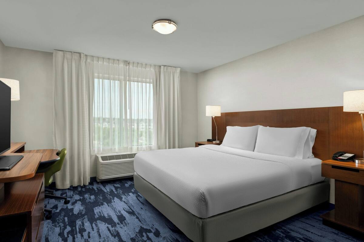 A hotel room with a large bed, a desk with a chair, a TV, and a window with curtains.