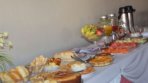 A buffet table with various food items including fruits, pastries, and a cake. - Hotel e Restaurante Residencial (Montes Claros)