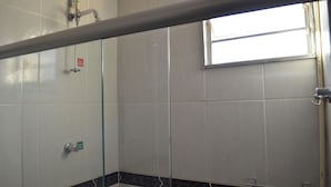 A bathroom with white tiles, a glass shower enclosure, and a window. - Hotel e Restaurante Residencial (Montes Claros)