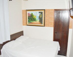 Una habitación con cama, un cuadro, una pared de ladrillo y una puerta de madera.
