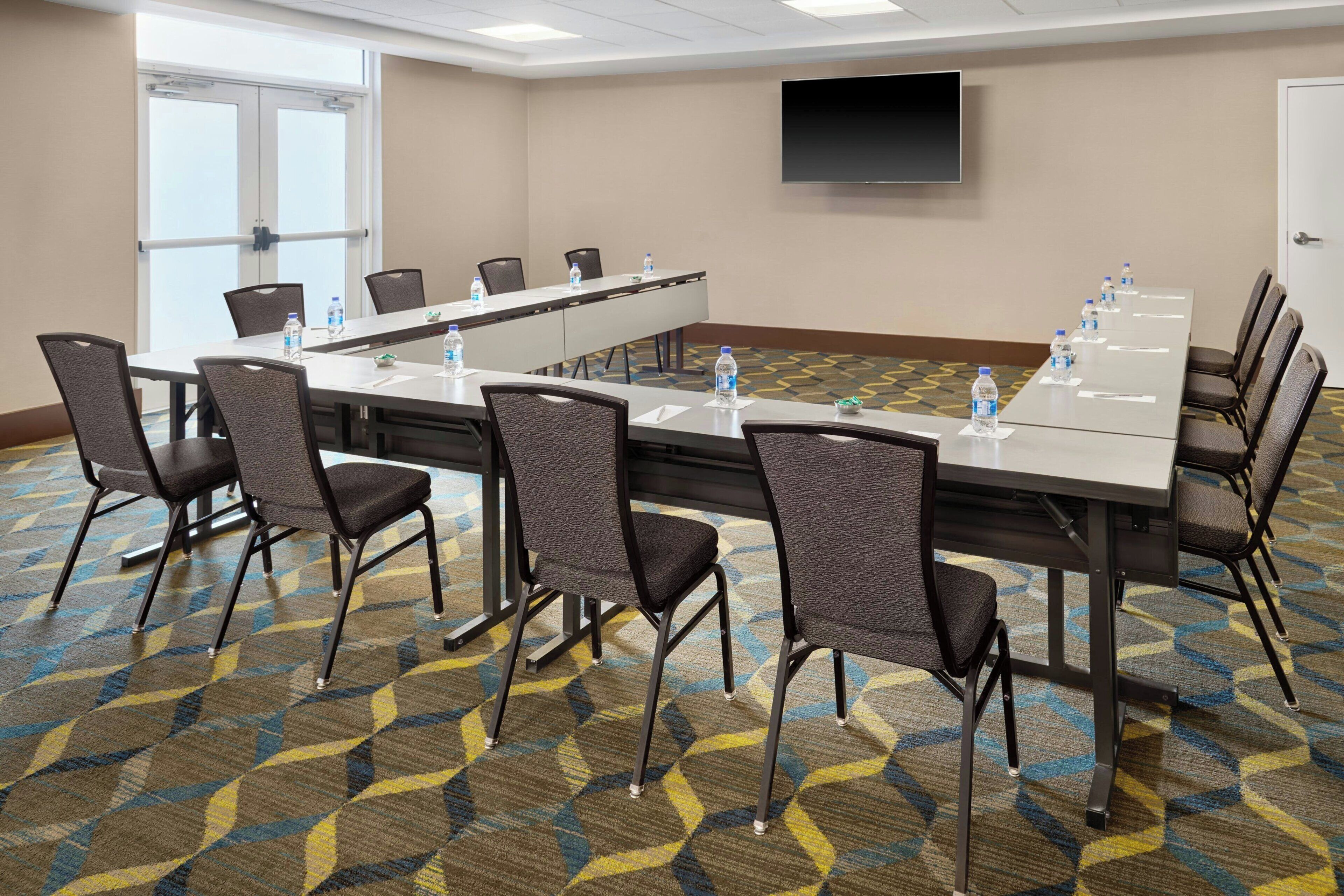 A conference room with a long table, chairs, water bottles, a TV, and patterned carpet.