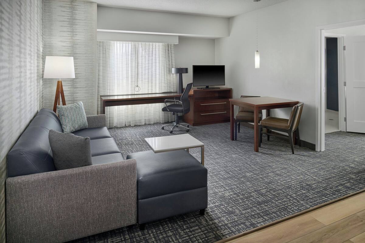 A modern living room with a sofa, a TV, a desk, and a dining table.