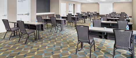 A conference room with multiple tables and chairs, a projector screen, and a carpeted floor.
