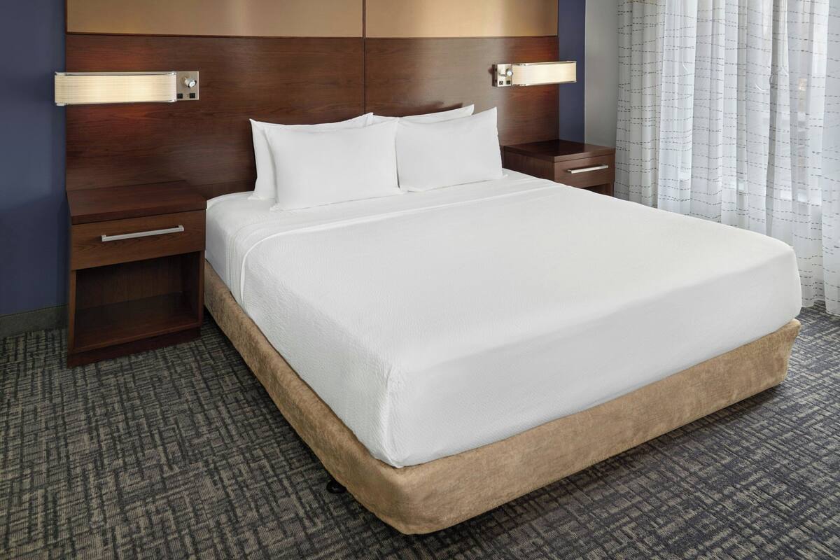 A hotel room with a large bed, wooden headboard, bedside tables, and a patterned carpet.