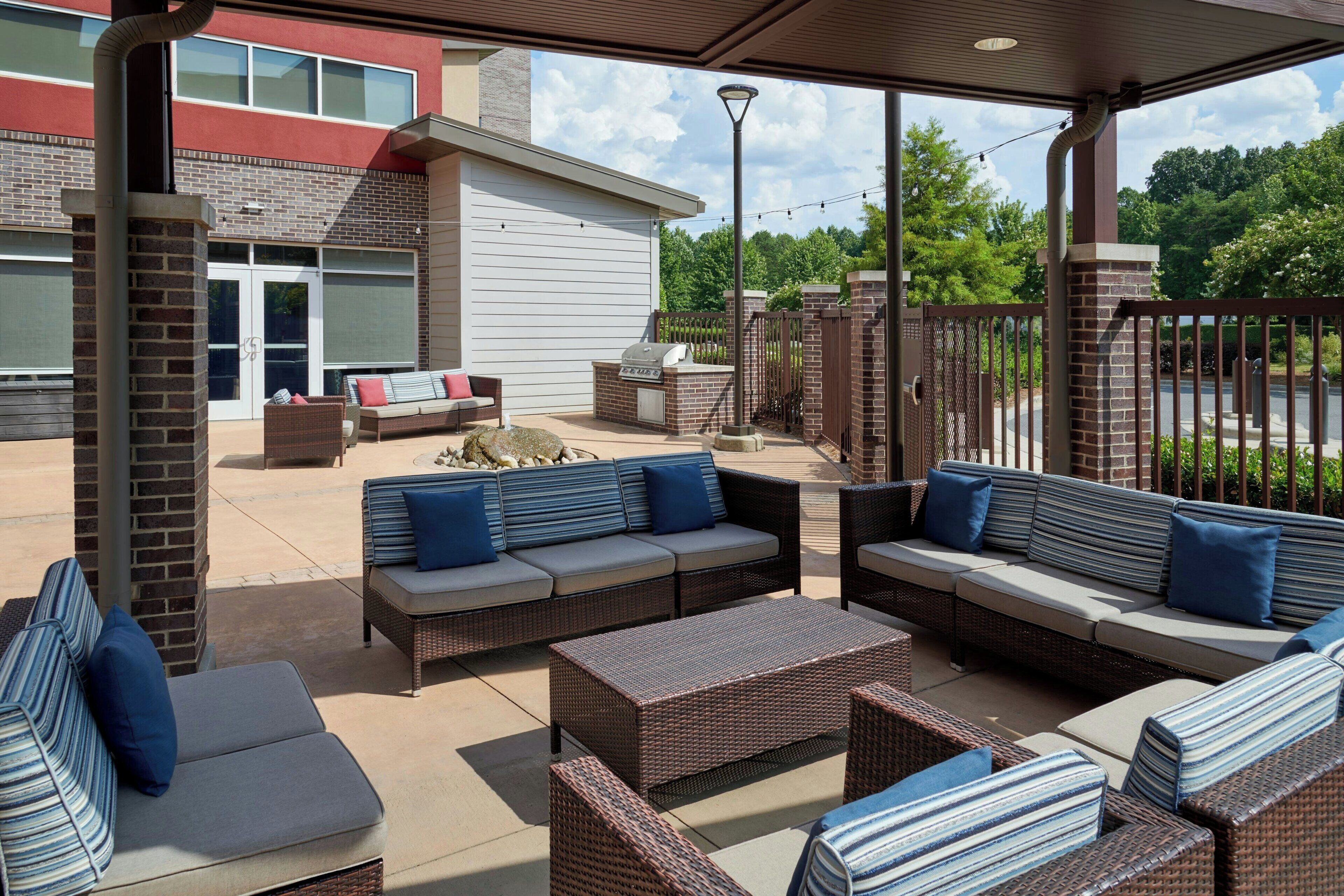 An outdoor patio area with wicker furniture, a grill, and a view of a building with a brick facade.
