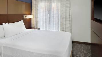 A hotel room with a large bed, a nightstand with a lamp, a TV mounted on the wall, and a window with curtains.