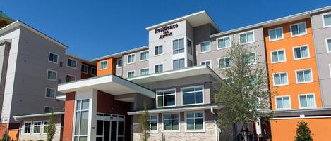 A multi-story hotel with a modern design, featuring a central entrance with a covered walkway, and a variety of room layouts visible through the windows.