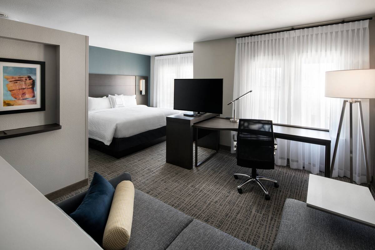 Una camera d'albergo con un letto, una scrivania con un computer, una TV, una lampada e un divano.