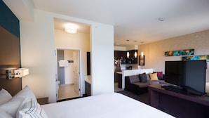 Ein Hotelzimmer mit Bett, Schreibtisch mit Fernseher, einer Küchenzeile und einem sichtbaren Badezimmer durch eine geöffnete Tür.