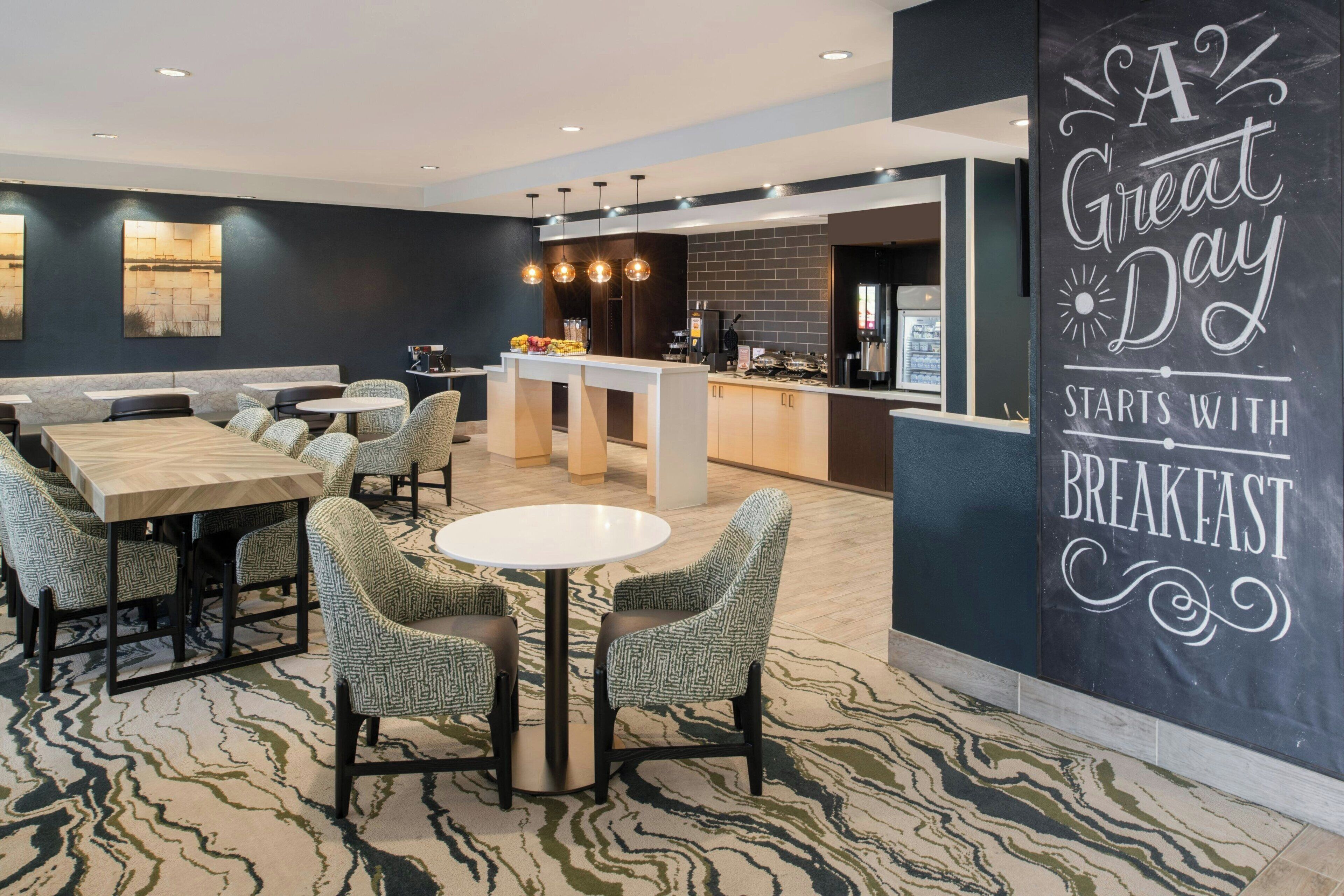 A modern breakfast area with seating arrangements, a counter, and a wall with a motivational quote.