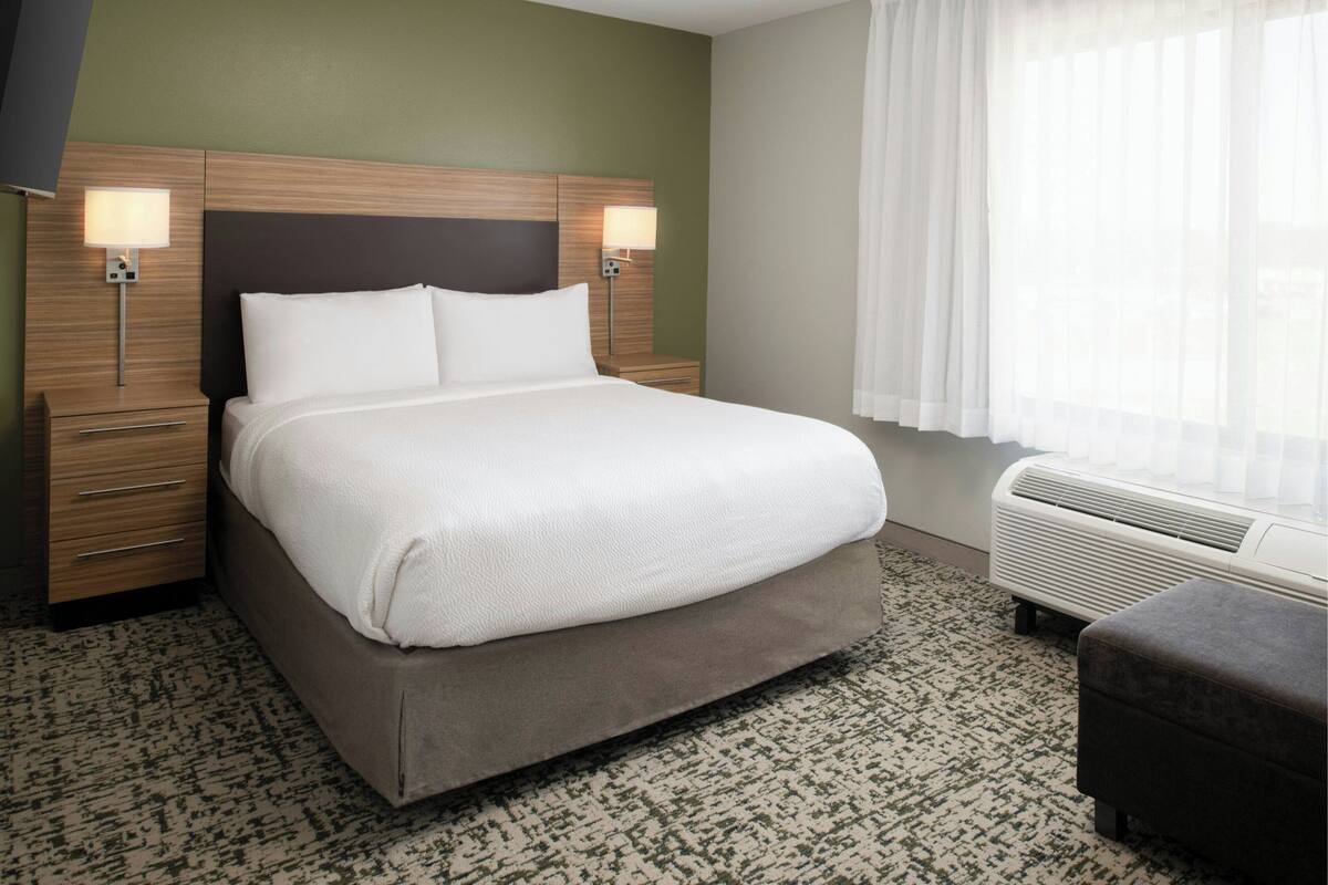 A hotel room with a large bed, bedside lamps, a heater, and a window with curtains.