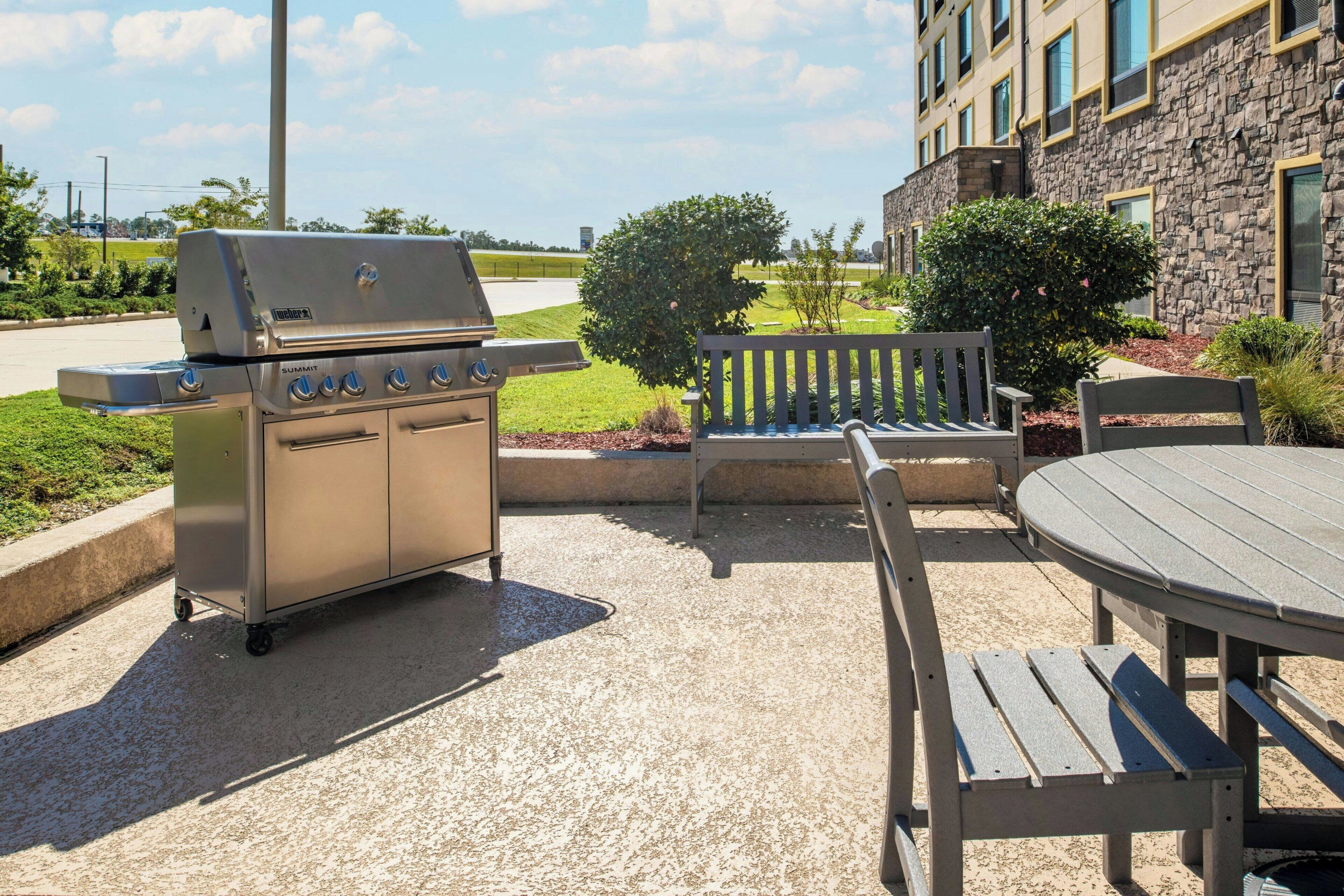 Une terrasse extérieure équipée d’un barbecue en acier inoxydable, d’un banc en bois et d’une table ronde.
