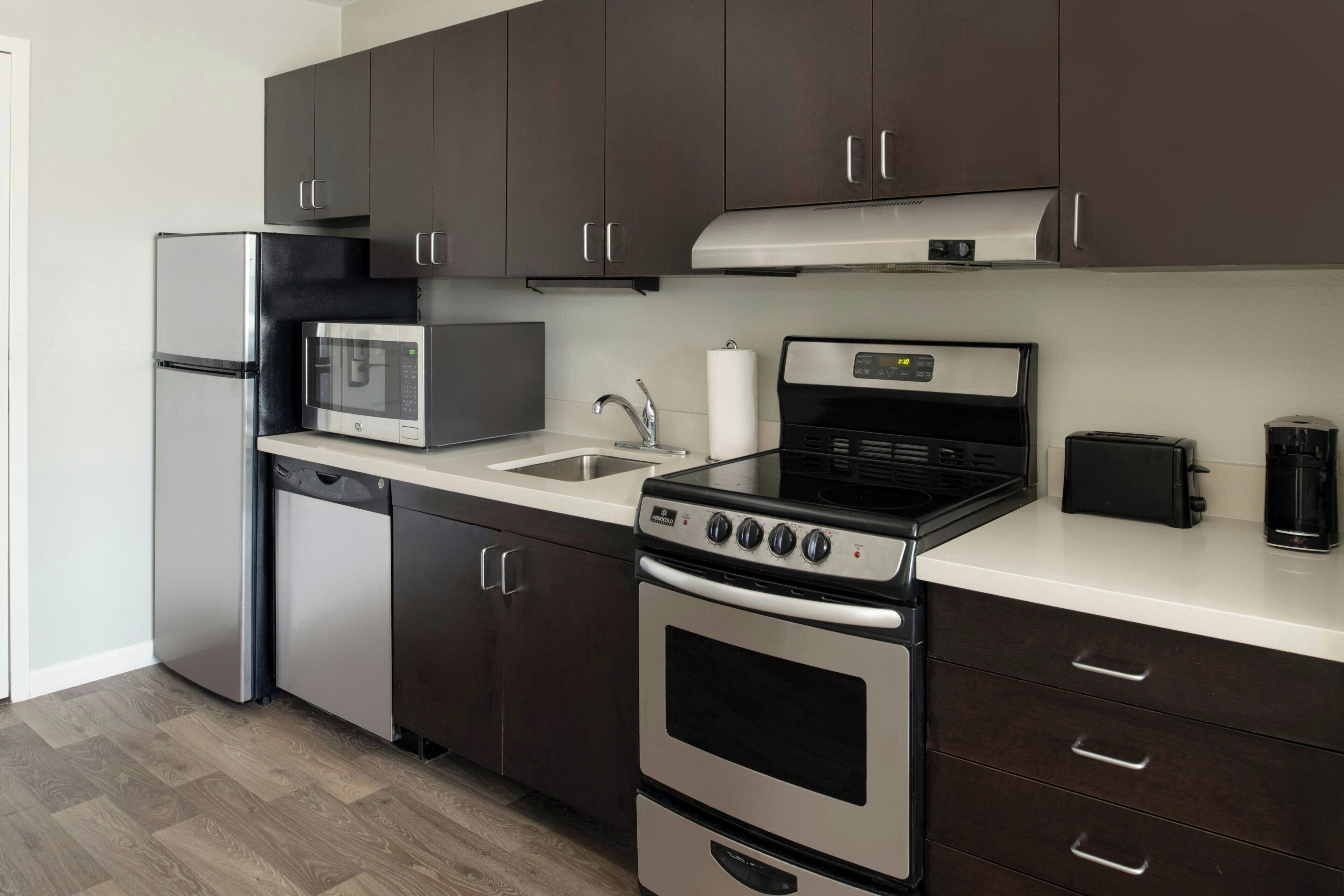 A modern kitchen with dark cabinets, stainless steel appliances, a dishwasher, a microwave, a stove, and a coffee maker.