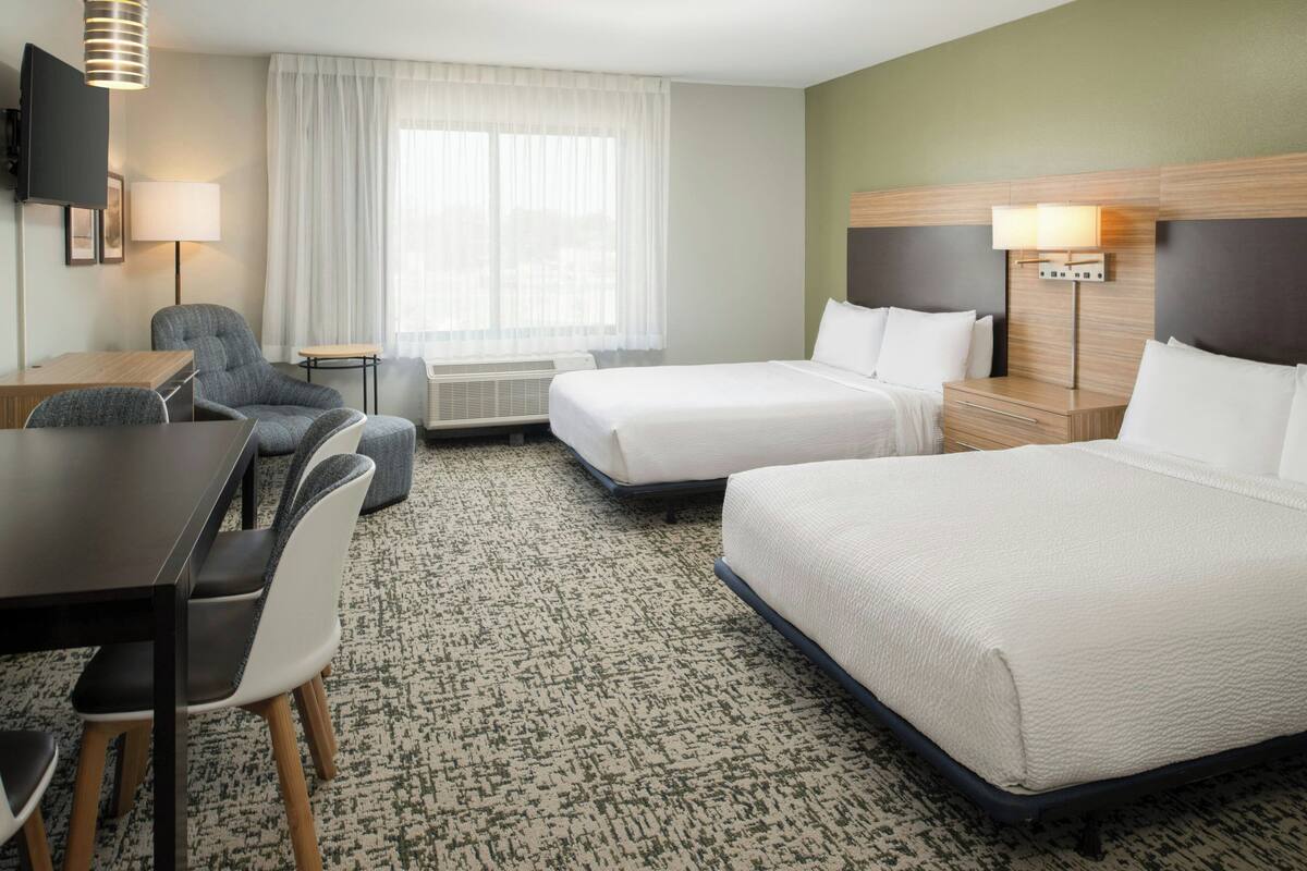 A hotel room with two beds, a desk, a chair, a TV, and a window with curtains.