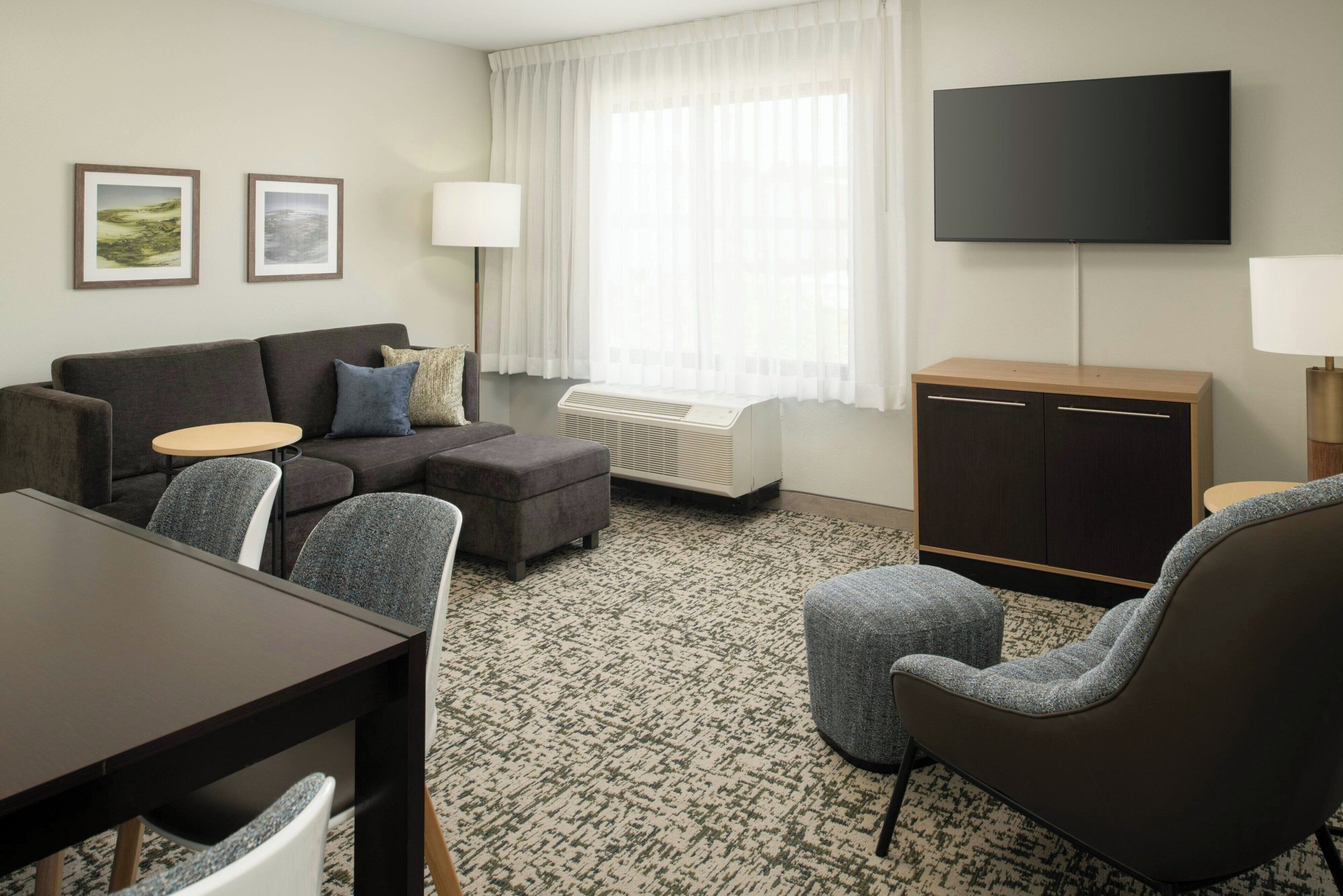 Een moderne hotelkamer met een bank, fauteuil, eettafel en een flatscreen televisie aan de muur.