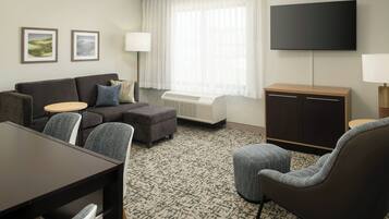 Een moderne hotelkamer met een bank, fauteuil, eettafel en een flatscreen televisie aan de muur.